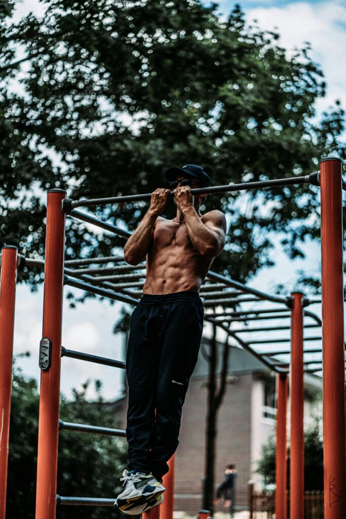 Athletic man performing pull-ups on a bar outdoors, showcasing fitness and strength.
